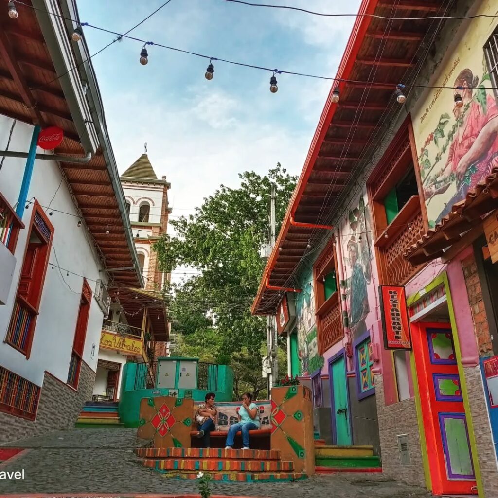 Calle peatonal con murales y bancas en Ciudad Bolívar, con la torre de la iglesia al fondo