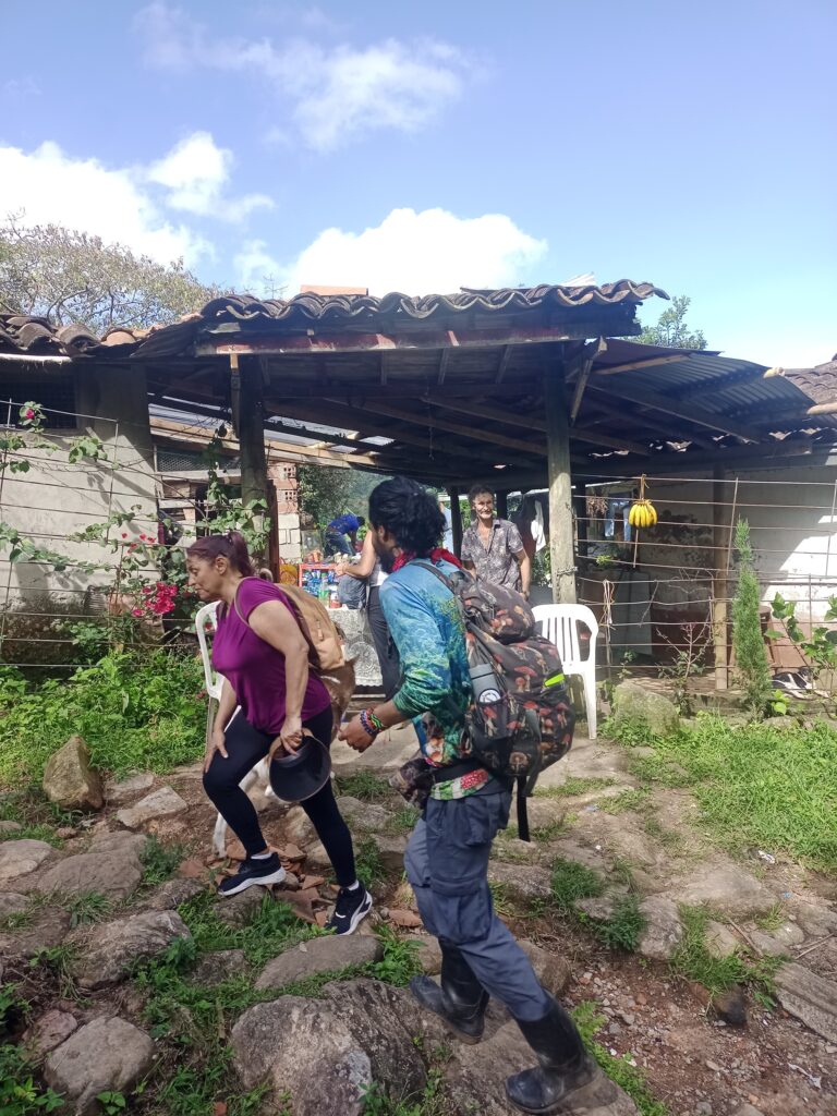 Caminantes sobre un camino arriero rocoso con una casa campesina al fondo.