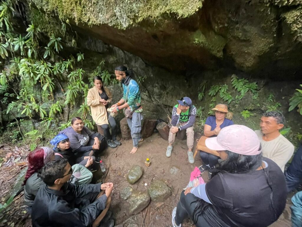 Senderistas descansando después de ingresar a una cascada, sentados en troncos alrededor de rocas.