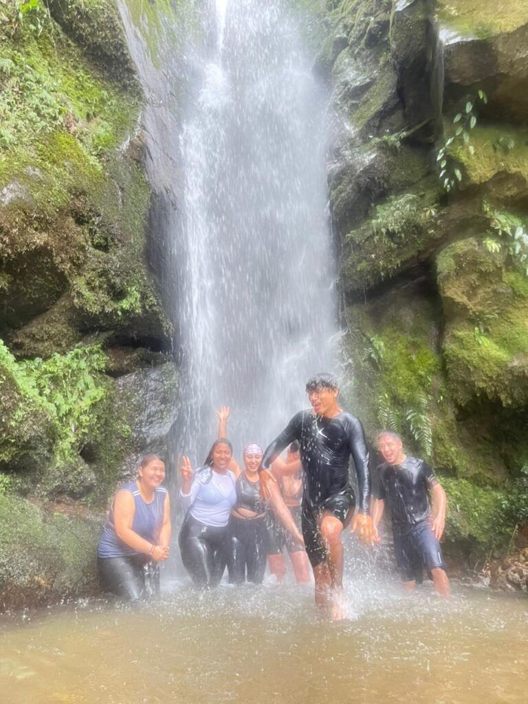 Grupo de caminantes reunidos bajo una cascada al final de la ruta.