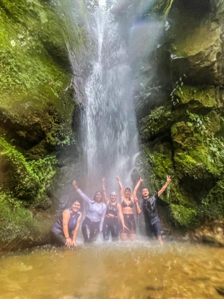 Grupo de caminantes tomándose una foto bajo una cascada.